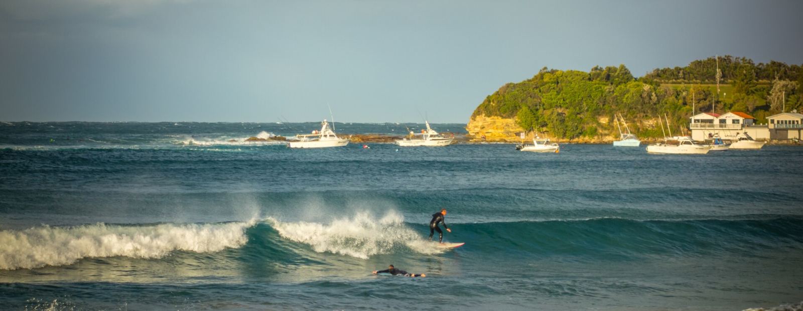 A surfer on a wave at Terrigal Beach, the headland behind